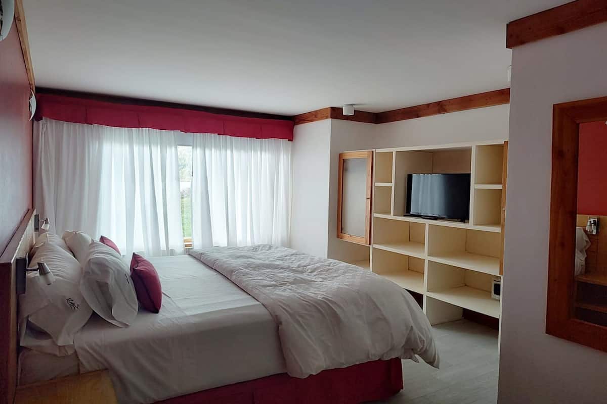 Una habitación de hotel con cama, televisor en un estante y ventana con cortinas.