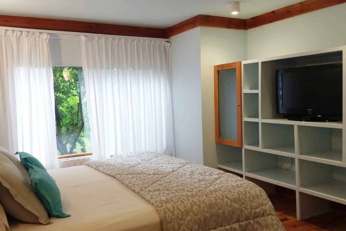 Un dormitorio con una cama, un televisor en un estante y una ventana con cortinas.
