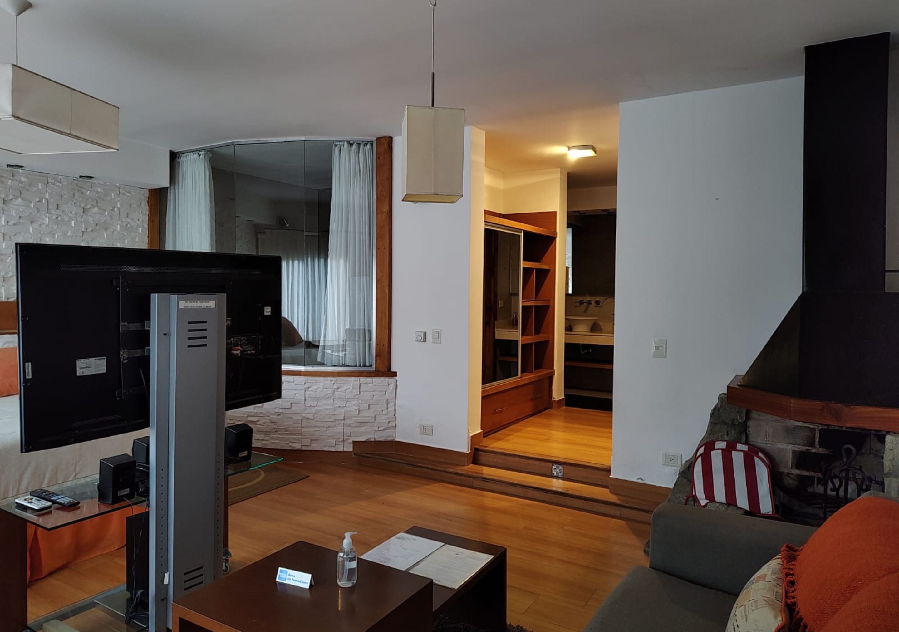 A modern living room with a flat-screen TV, a coffee table, and a sofa. There is a fireplace and a staircase leading to a loft area.