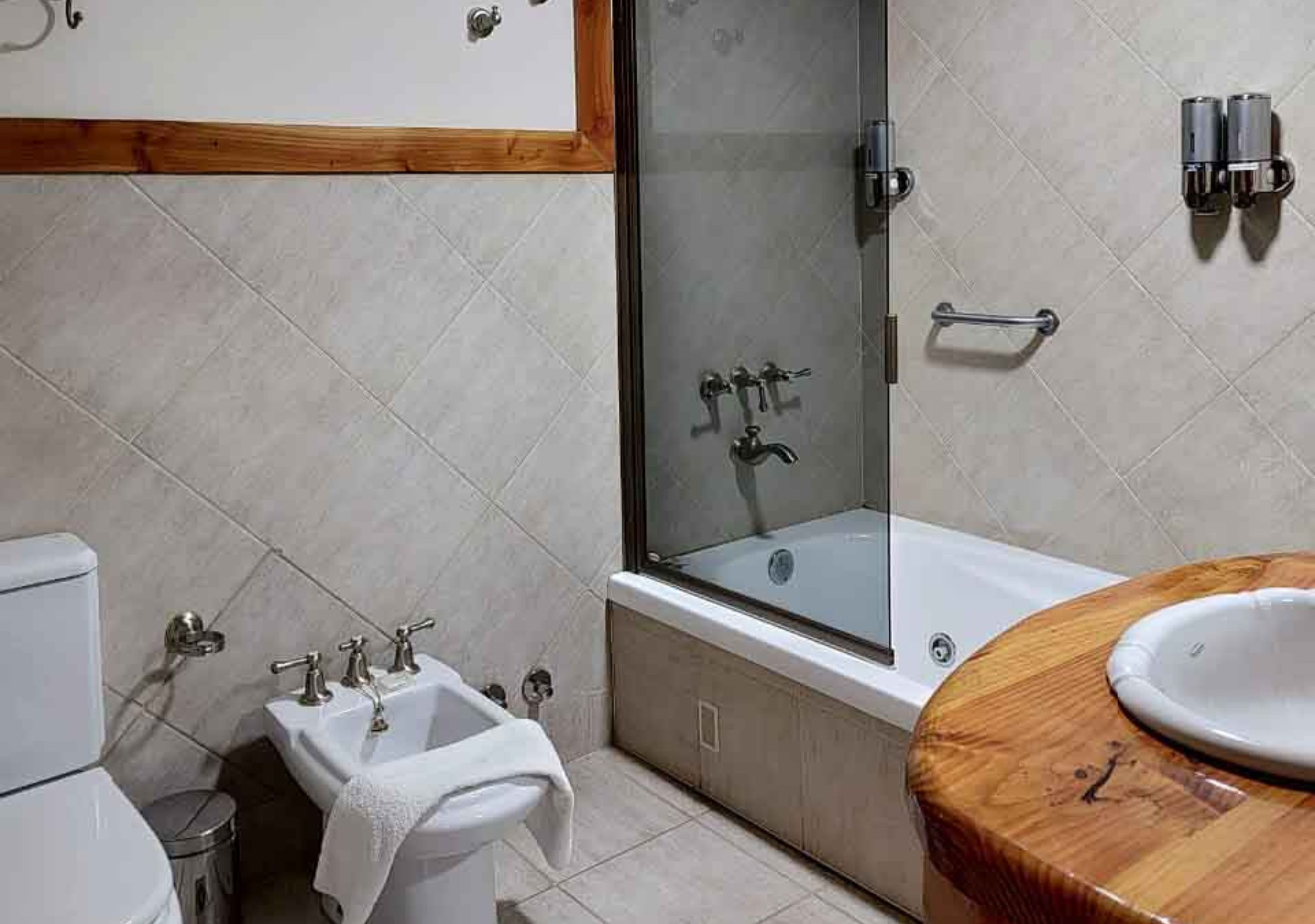 Un baño moderno con ducha envuelta en vidrio, tocador de madera y lavamanos blanco.