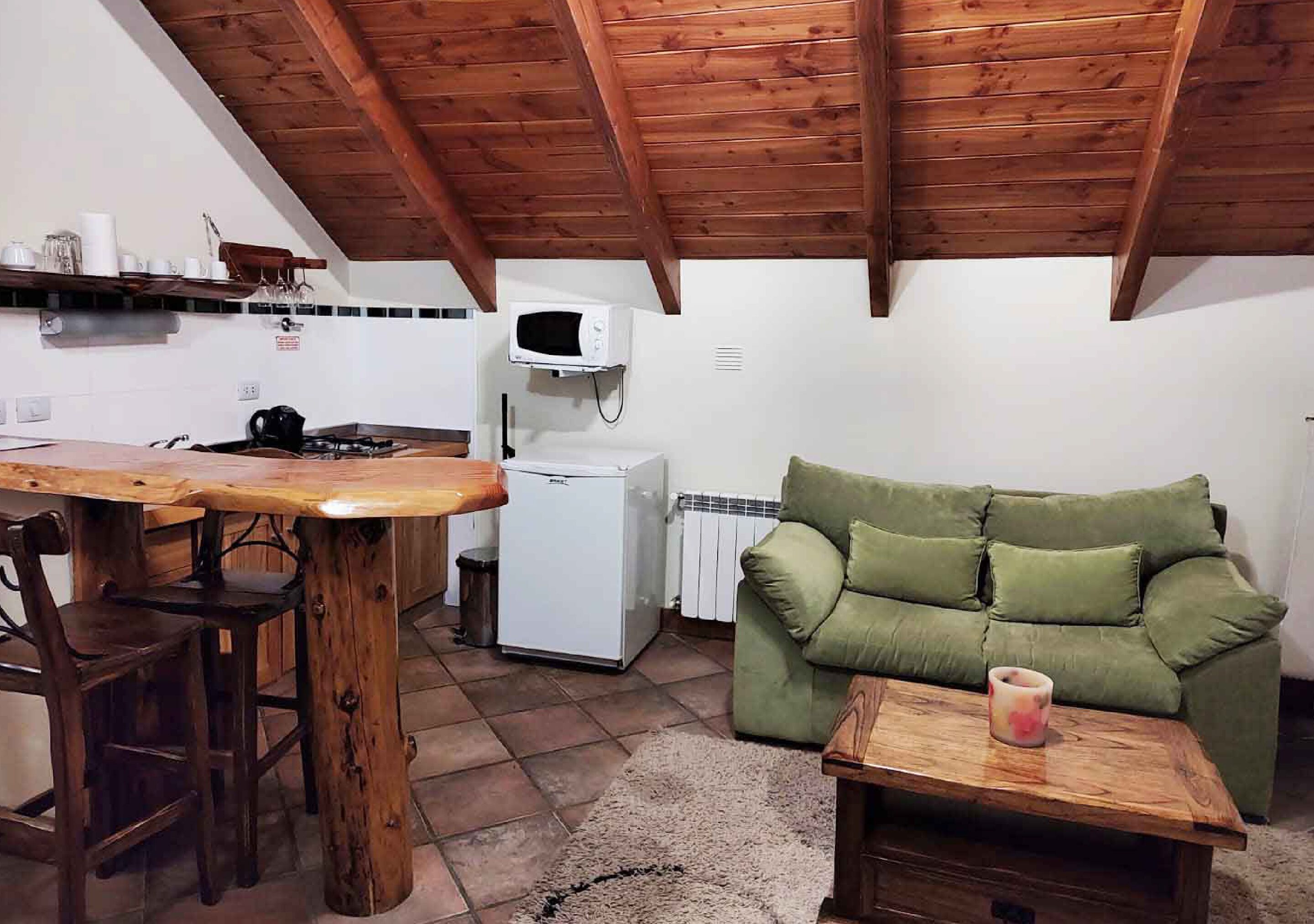 Een compacte keuken met houten balken, een magnetron, een kleine koelkast en een groene bank.