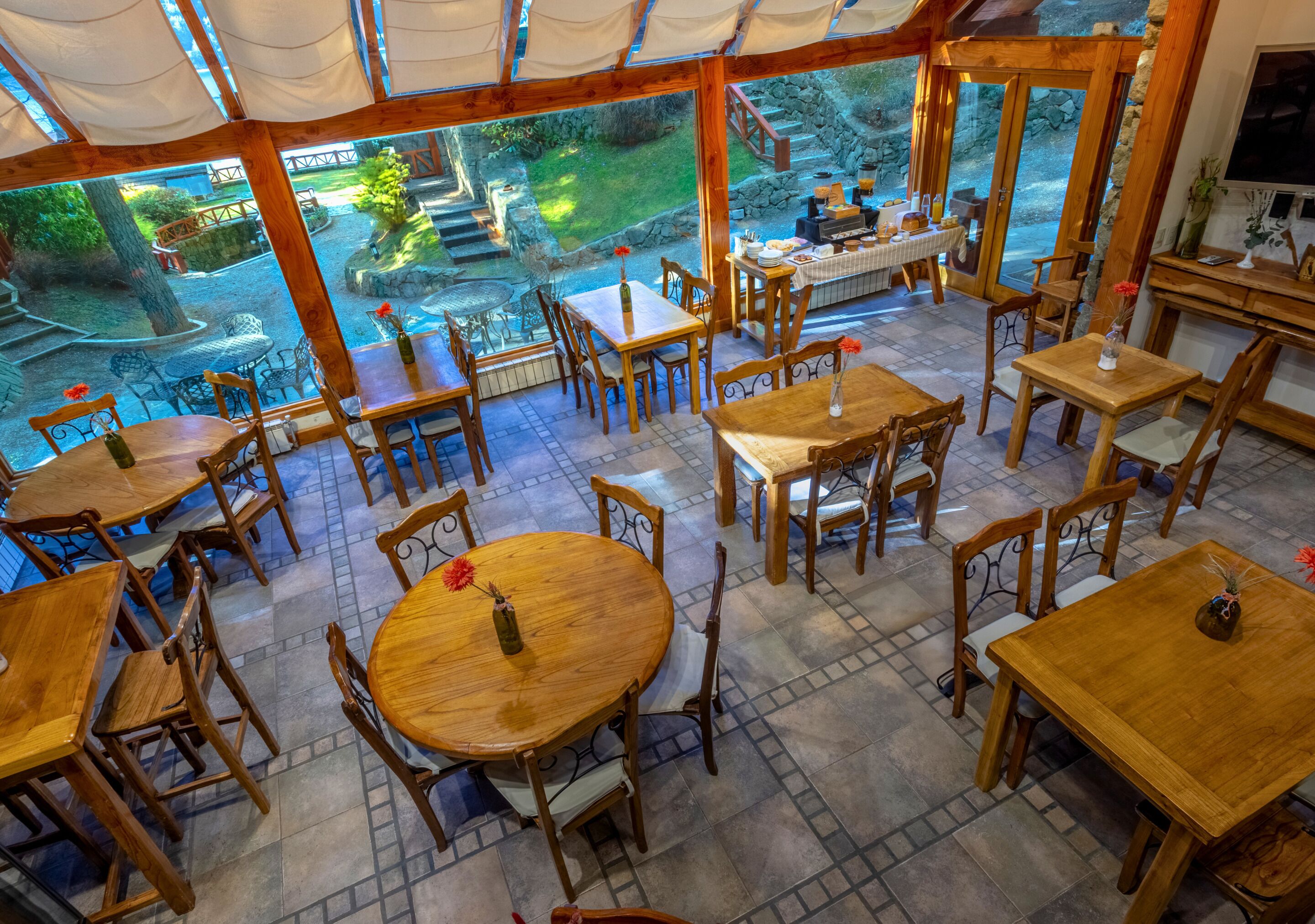 Un restaurant avec des tables et des chaises en bois, une fontaine en pierre et une vue sur un jardin.
