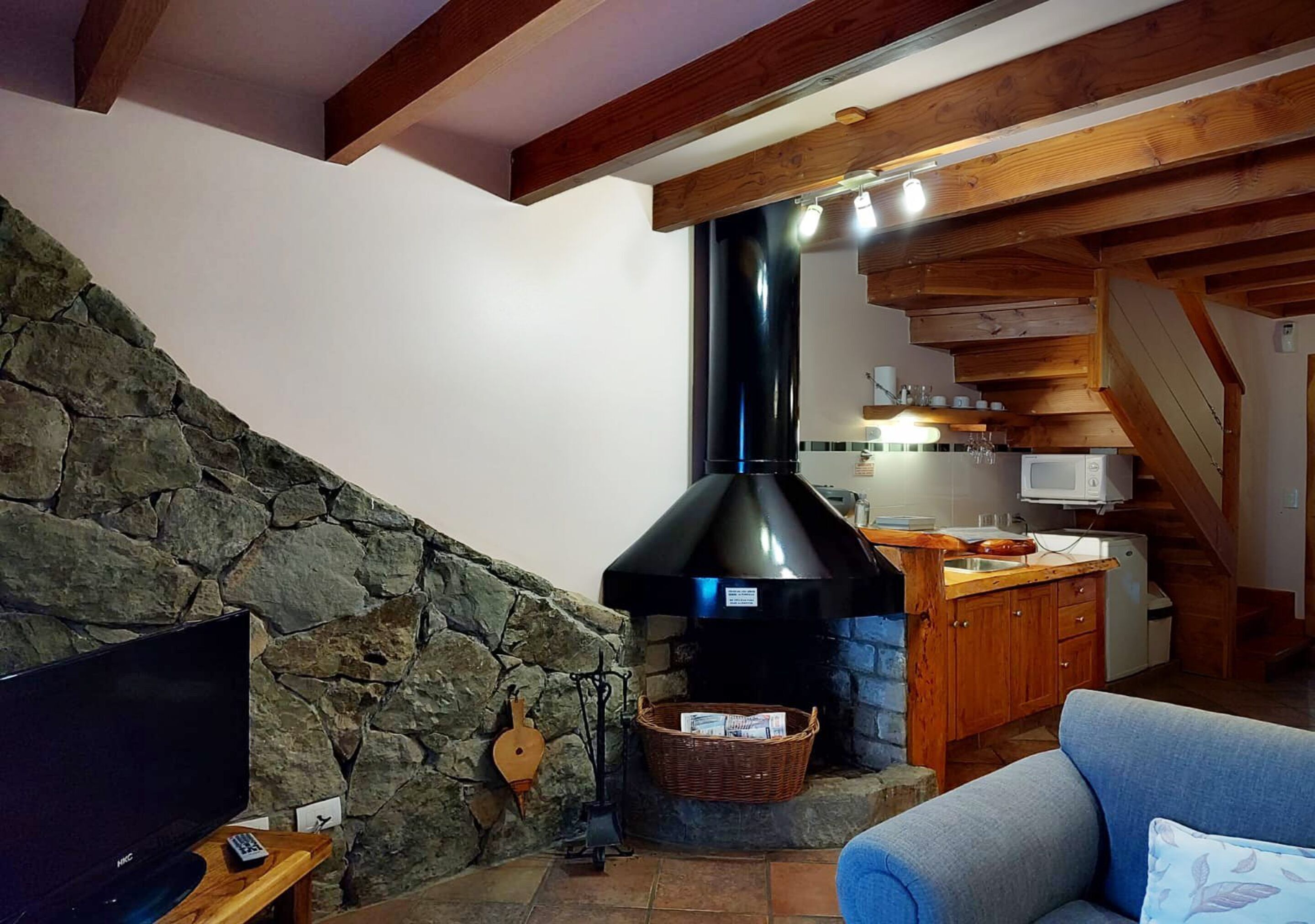Ein gemütliches Wohnzimmer mit Steinwand, Kamin, Fernseher und blauem Sofa.