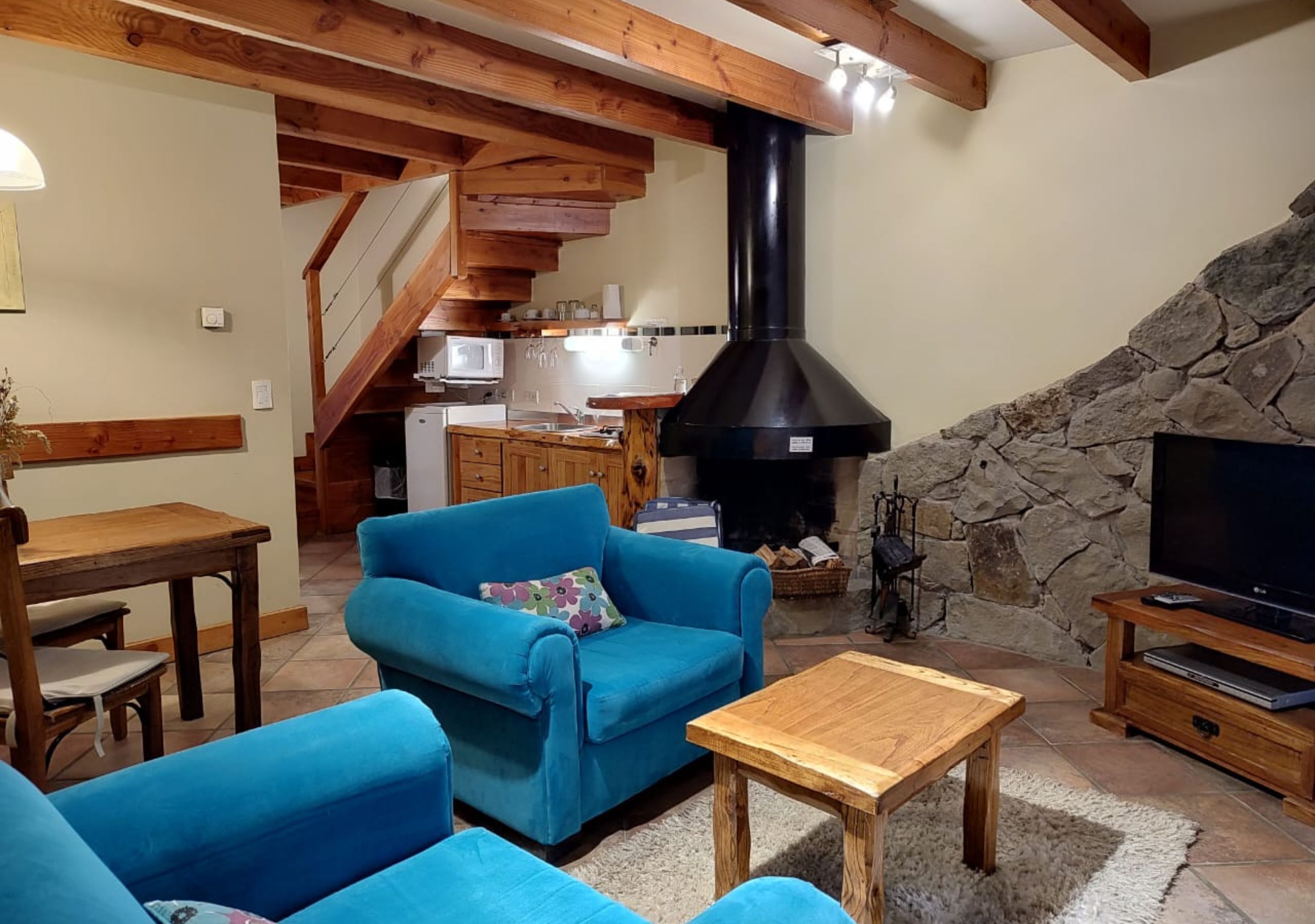 Un salon chaleureux avec un canapé bleu, une table basse en bois, une cheminée en pierre et un téléviseur.