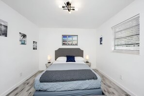 Quarto moderno com uma cama grande, vista para a praia e uma janela com persianas.