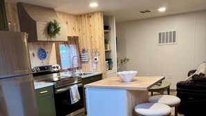 Une cuisine moderne avec des armoires en bois, un réfrigérateur en acier inoxydable et un four encastré. On y trouve un petit îlot avec des tabourets et un évier blanc.