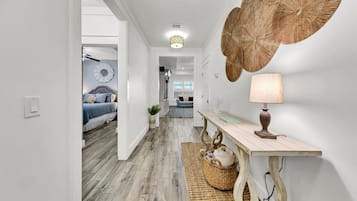 Een hal met een houten vloer, een witte muur met een groot decoratief paraplu, een tafel met een lamp, en een bed met blauw beddengoed op de achtergrond.