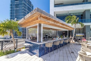 Ein Außenbereich mit Bar, überdacht von einer Holz-Pergola, Barhocker und gefliestem Boden.