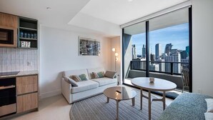 Una sala de estar moderna con vistas a la ciudad, un sofá, una mesa de centro y una zona de cocina con armarios y encimera.