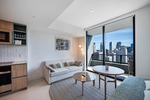 Ein modernes Wohnzimmer mit Blick auf die Stadt, inklusive Sofa, Couchtisch und einer Küchenzeile mit Schränken und einer Arbeitsplatte.