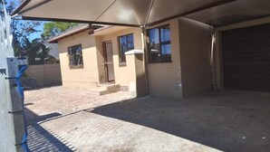 A covered outdoor area with a brick floor, a small building with a door and windows, and a garage door. - Duminy Guest Lodge (Duminy Street)