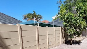 A paved pathway with a beige fence and a tree. - Duminy Guest Lodge (Duminy Street)
