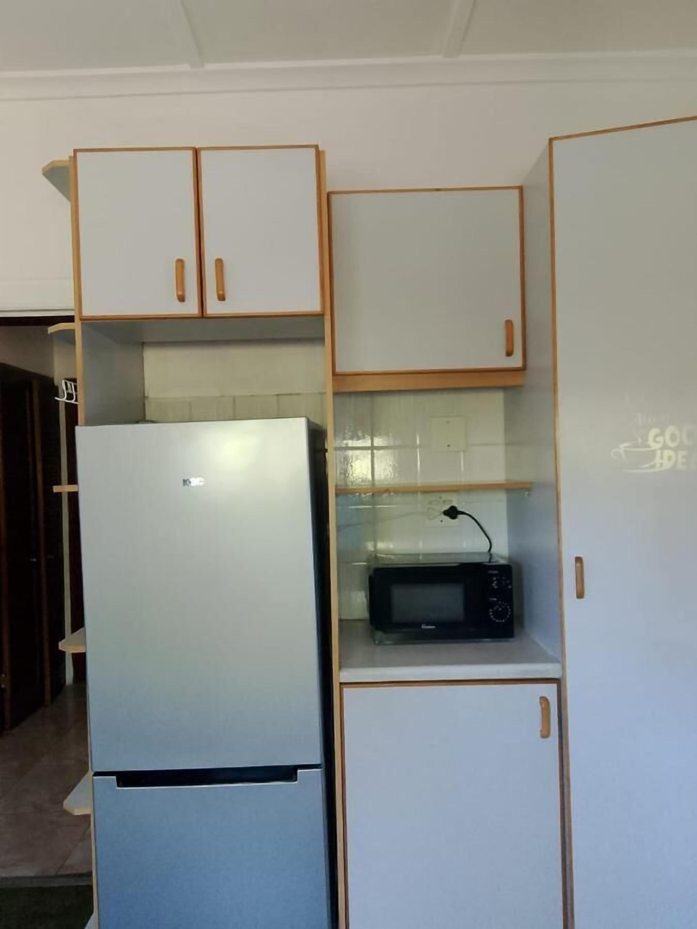 A compact kitchen with a refrigerator, microwave, and wooden cabinets.