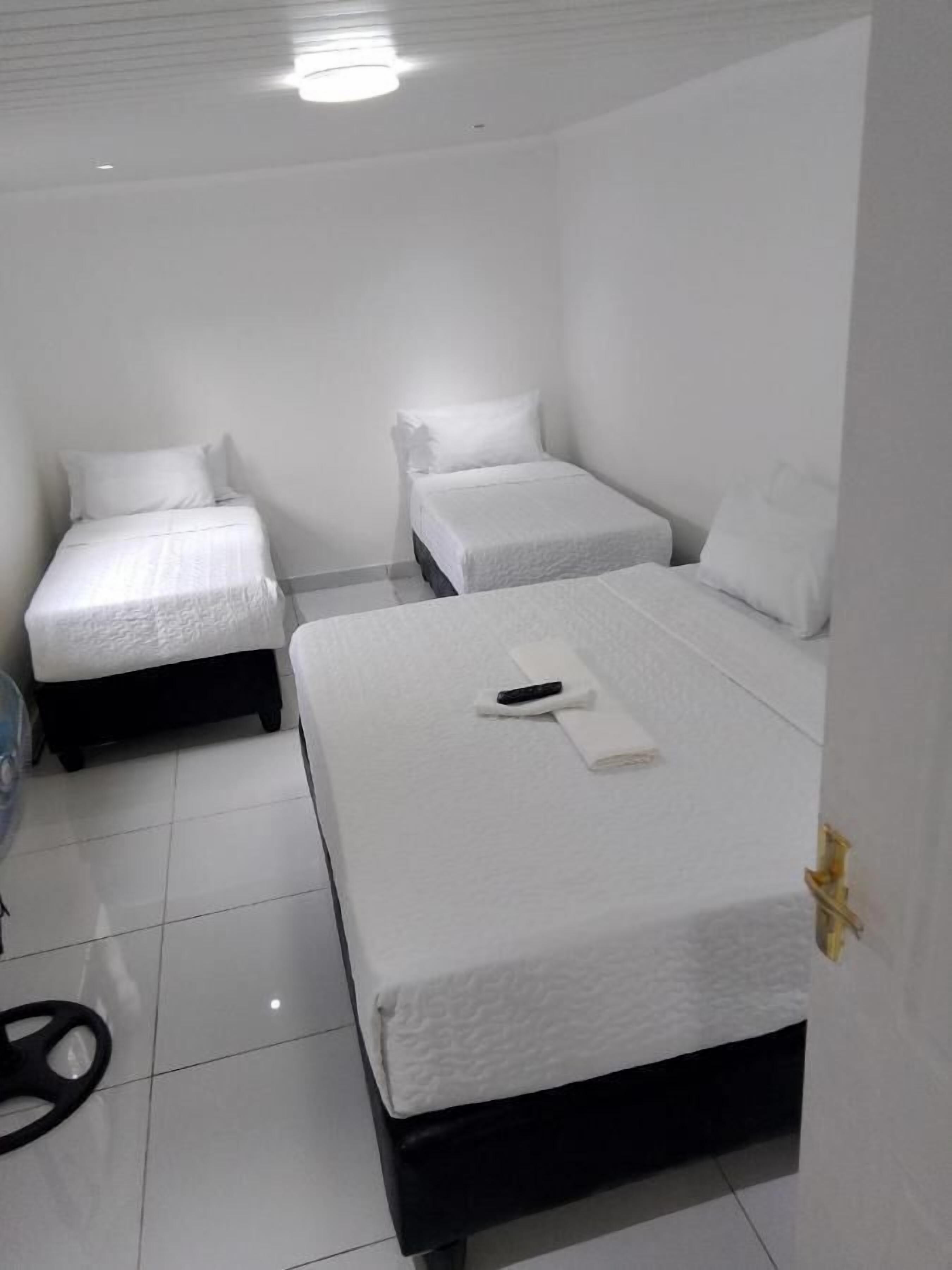 Una habitación limpia y blanca con dos camas individuales y una cama más grande.
