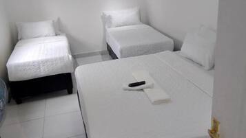 Una habitación limpia y blanca con dos camas individuales y una cama más grande.