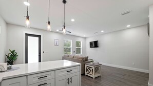 Une cuisine moderne avec des armoires blanches, un grand îlot central, des luminaires suspendus et un ventilateur de plafond.