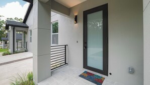Une façade moderne avec une porte vitrée, une rambarde en métal et un paillasson.