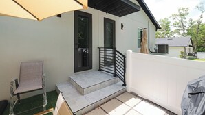 Un espace extérieur abrité, avec une chaise, des marches menant à une porte et une clôture blanche.