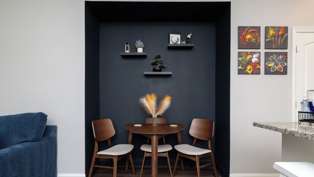 A modern dining area with a round table, four chairs, and a vase with feathers.