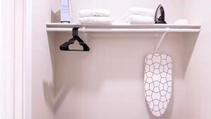 Ett badrum med en vit hylla där en vit handduk, en svart galge och ett vitt strykjärn står.
