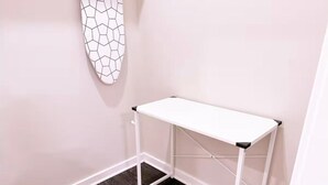 Ett vitt skrivbord i metall med en svart skiva, placerat i ett hörn mot en vägg, och ovanför det hänger ett konstverk med ett geometriskt mönster.