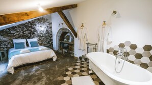 A bedroom with a large bed, a bathroom with a bathtub, and a stone wall.