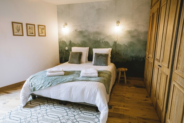 A bedroom with a bed, a wall-mounted light, a wooden wardrobe, and a patterned rug. - Charming House with a Spa• Heart of Bergerac (Bergerac)
