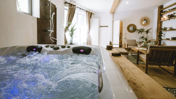 A hot tub with water jets, a wooden bench, and a dining area with a table and chairs.