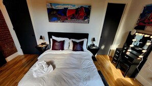 Un lit bien fait, avec du linge de lit blanc et un ensemble de serviettes, une tête de lit noire et un tableau au-dessus du lit.