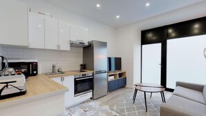 Una cocina moderna con armarios blancos, microondas, tostadora, refrigerador y horno empotrado.