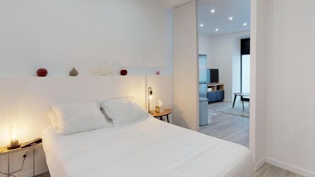 A modern hotel room with a bed, bedside table, lamp, and a view of the dining area. - Luxurious and Cosy Apt in The Center of Paris 14 (Paris)