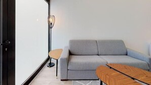 Una sala de estar moderna con un sofá gris, una mesa de centro de madera, una mesita redonda pequeña y una lámpara de pie.