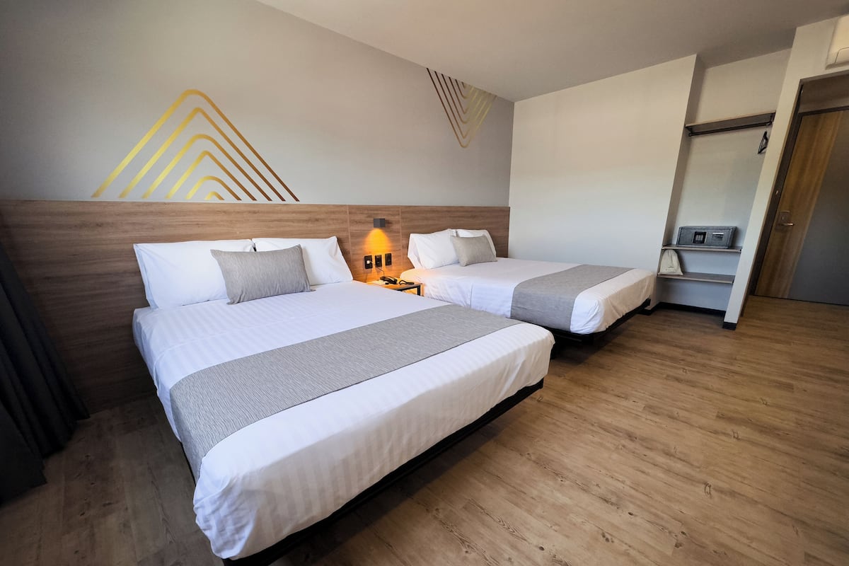 Habitación de hotel con dos camas, suelo de madera, una lámpara fijada a la pared y una puerta con panel de control.