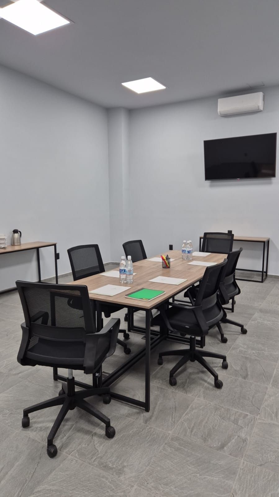 A conference room with a long table, black chairs, water bottles, and a flat-screen TV on the wall.