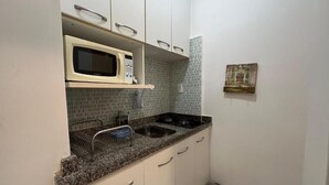 Una cocina compacta con armarios blancos, microondas, fregadero y cubo de basura.