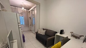 Un espacio habitable compacto con kitchenette, un sofá, un comedor y una puerta corrediza que da a un baño.
