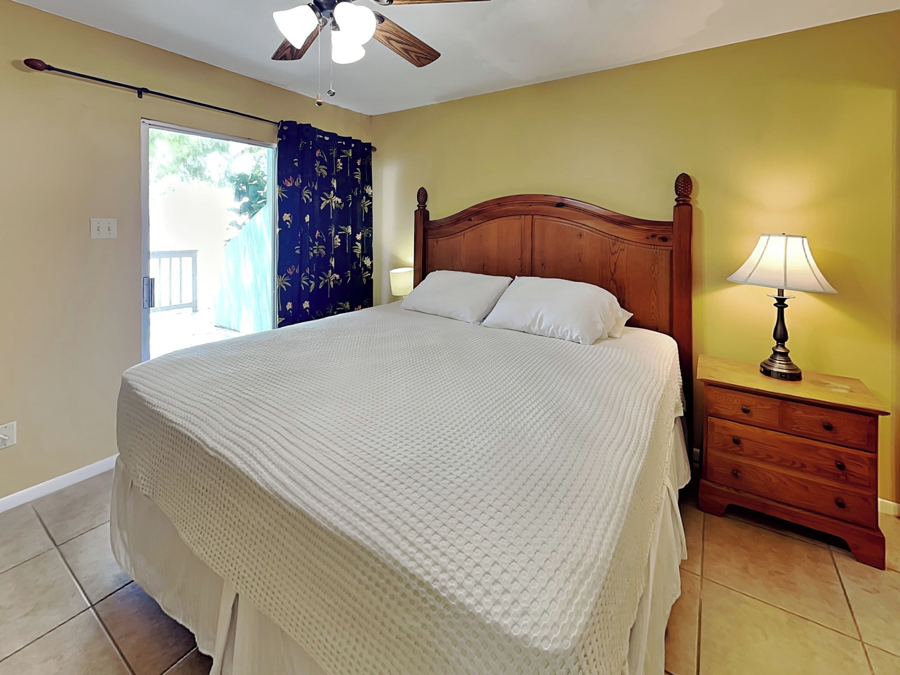 A bedroom with a wooden bed, a nightstand with a lamp, and a ceiling fan.
