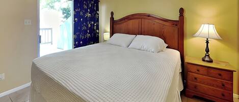 A bedroom with a wooden bed, a nightstand with a lamp, and a ceiling fan.