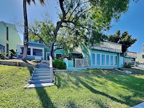 A two-story house with a front porch, a staircase leading to the entrance, and a well-maintained lawn. - Watercolor Skies by Silver Sands Vacation Rentals (Port Aransas)