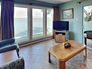 A living room with a large window, a television, and a wooden coffee table. - Watercolor Skies by Silver Sands Vacation Rentals (Port Aransas)