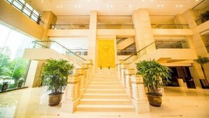 Ein mehrgeschossiges Interieur mit einer zentralen Treppe, Glasgeländern und Blumentöpfen.