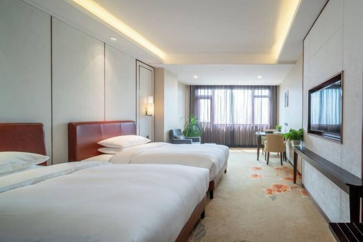 A hotel room with two beds, a desk, a chair, and a TV.