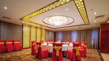 Un salón de banquetes con mesas redondas, sillas rojas con lazos dorados y una araña de cristal.