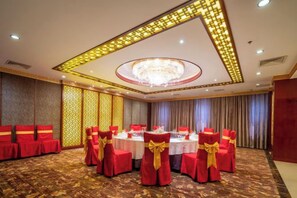 A banquet hall with round tables, red chairs with gold sashes, and a chandelier. - Guanghua International Hotel (Nantong)