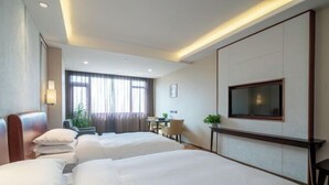 Ein Hotelzimmer mit zwei Betten, einem Schreibtisch, einem Stuhl, einem Fernseher und einem Fenster mit Vorhängen.