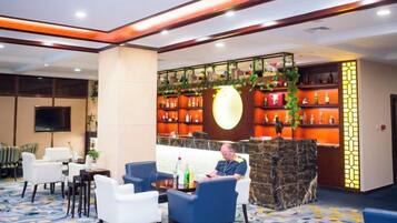 A lobby with a reception desk, seating area, and a bar with shelves of bottles.