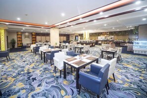 A hotel dining area with tables and chairs, a kitchen in the background, and a patterned carpet. - Guanghua International Hotel (Nantong)