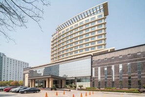 A multi-story hotel with a modern design, featuring a large glass facade and a parking area with orange traffic cones. - Guanghua International Hotel (Nantong)