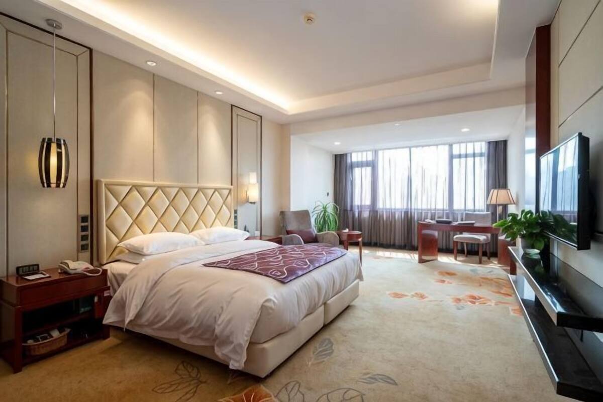 A hotel room with a large bed, bedside tables, a TV, and a desk with a chair.