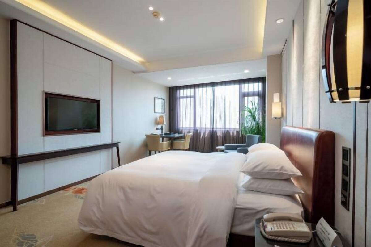 A hotel room with a large bed, a desk, a chair, a television, and a bedside telephone.